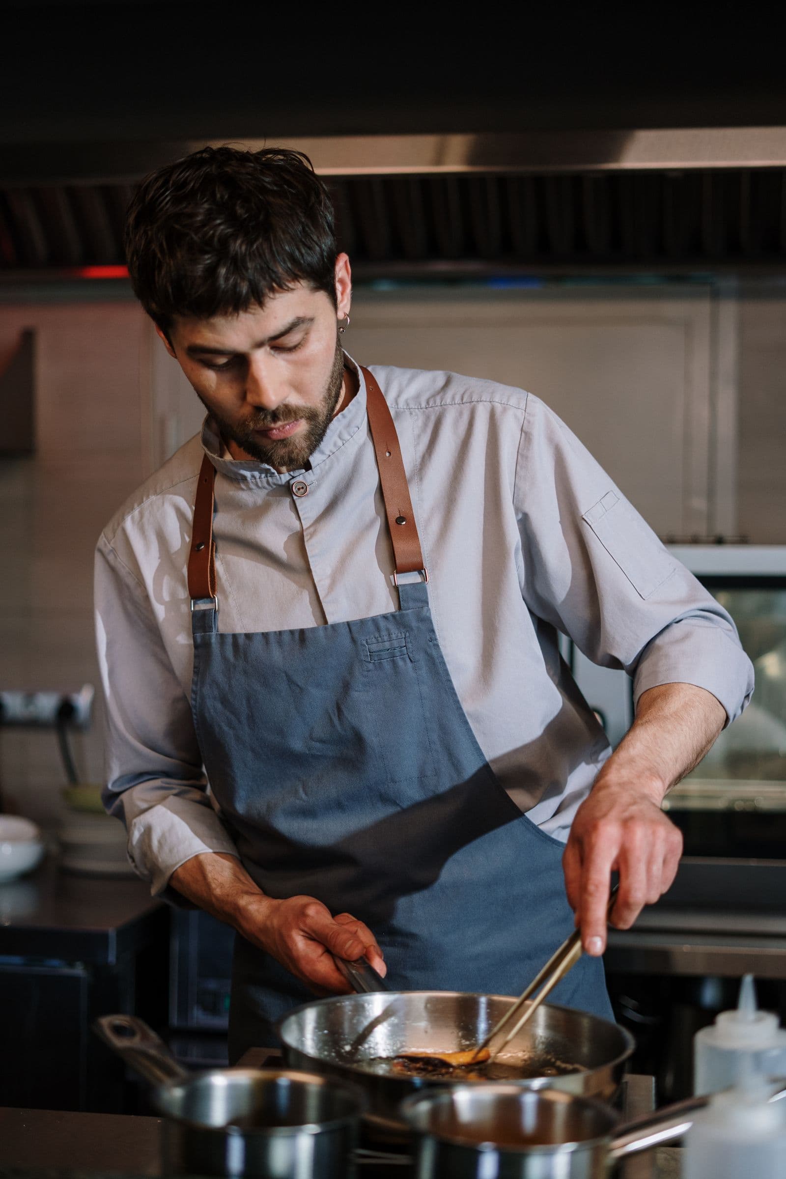 Cocinero con delantal azul y tirantes de cuero salteando en una cocina profesional