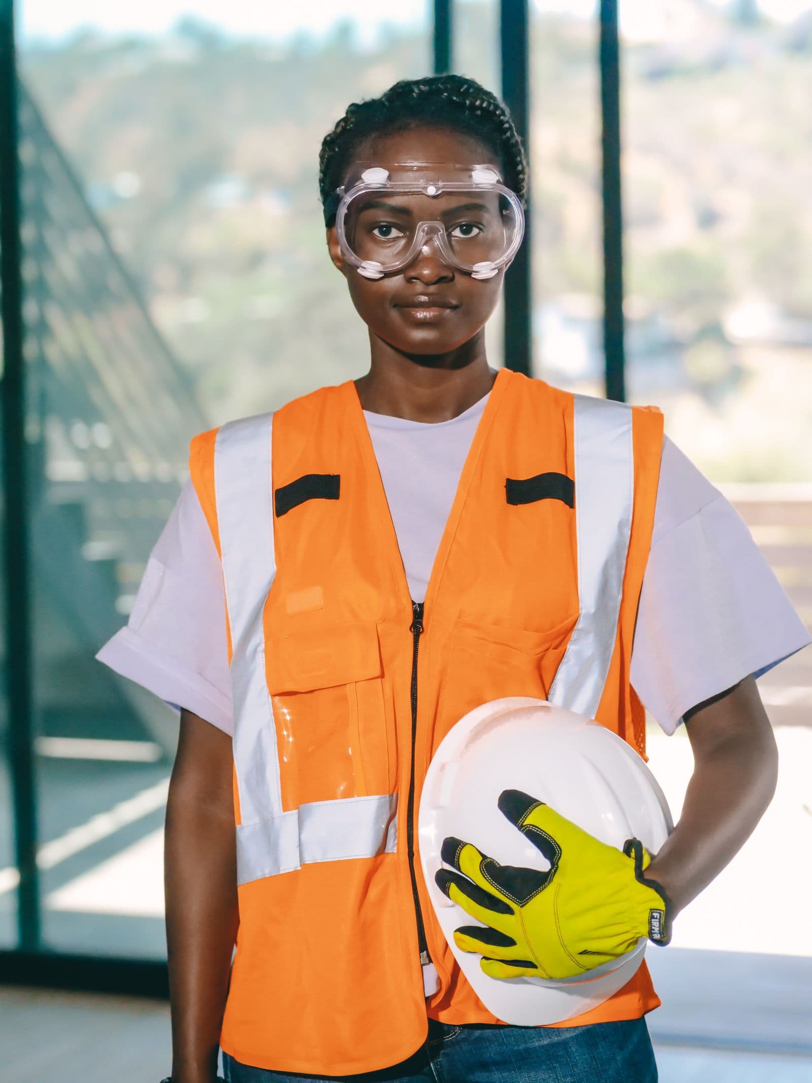 Trabajadora con chaleco naranja de alta visibilidad, gafas de protección y casco blanco en la mano